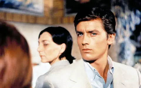 Alain Delon, icona di stile, in una scena che evoca i suoi film più belli. Sguardo intenso, fascino intramontabile.