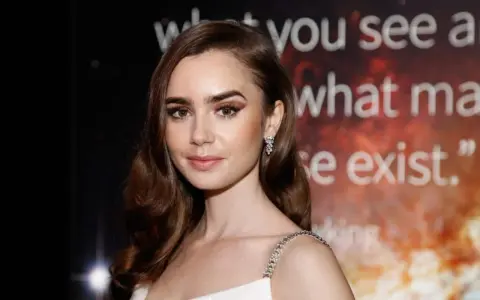 Lily Collins, protagonista di film e programmi TV, con un'espressione pensierosa e un abito scintillante.