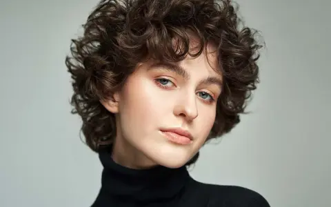 Modella con scalati tagli corti ricci, sguardo intenso e labbra naturali.