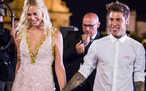 Fedez e Chiara sorridono, un momento speciale che ricorda la loro canzone. Lei indossa un abito scintillante, lui una camicia bianca.