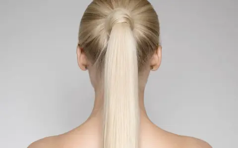 Vista posteriore di una donna con una **coda alta gonfia davanti**, capelli biondi lisci e spalle scoperte.