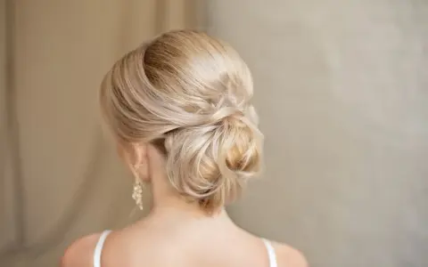 Chignon basso cerimonia con capelli biondi intrecciati, un'acconciatura elegante e raffinata per un'occasione speciale.
