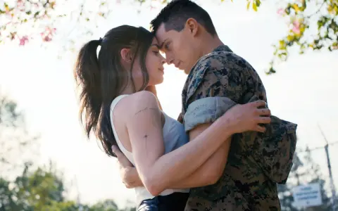 Nicholas Galitzine, in uniforme militare, abbraccia teneramente la sua fidanzata sotto un albero fiorito.
