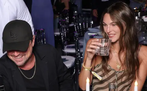 Vittoria Ceretti e Leonardo DiCaprio sorridono a una cena. Lei tiene un bicchiere, lui indossa un cappellino con la "LA".