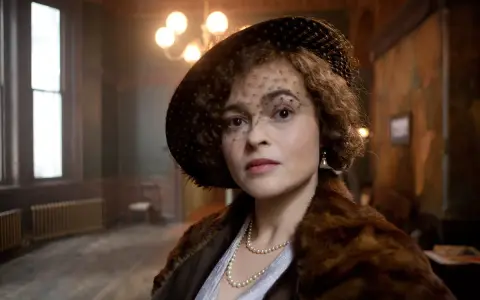 Helena Bonham Carter, con cappello e velo, indossa una pelliccia e perle. Scena da un film.