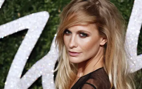 Donna con capelli sciolti eleganti, sguardo intenso e trucco deciso, sullo sfondo di un logo scintillante.
