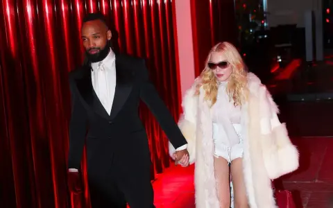 Madonna, con un cappotto di pelliccia bianco e un abito audace, cammina mano nella mano con il suo compagno, vestito elegantemente in smoking nero.