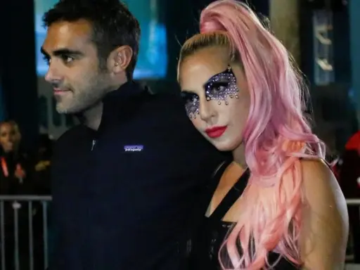 Lady Gaga con il suo fidanzato, Christian Carino, durante un evento. Lei indossa un trucco scintillante e capelli rosa.