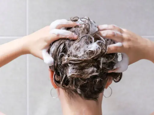 Mani che massaggiano shampoo sui capelli bagnati, schiuma abbondante. La domanda "ogni quanto lavare i capelli" è centrale per una chioma sana.