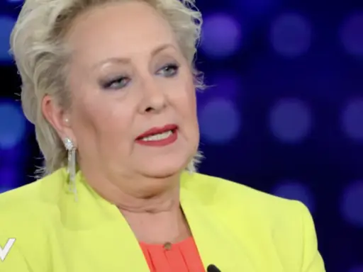 Carolyn Smith, come sta, con un tailleur giallo acceso e un top arancione, parla con un microfono.