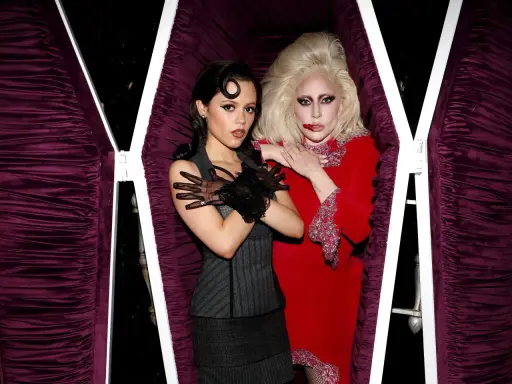 Jenna Ortega e Lady Gaga, parte del cast di Mercoledì, posano in una bara decorata con velluto viola.