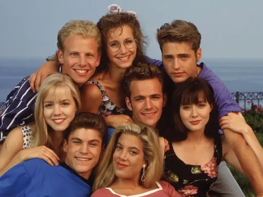Il cast di Beverly Hills 90210, un gruppo di amici sorridenti con lo sfondo del mare.