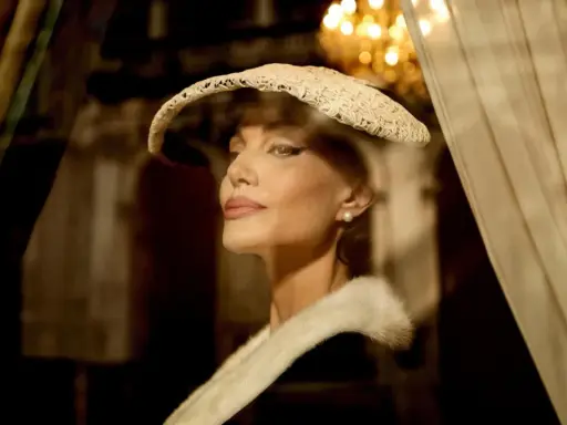 Angelina Jolie nei panni di Maria Callas, con un cappello di pizzo e una pelliccia, evoca l'eleganza di un'epoca passata.