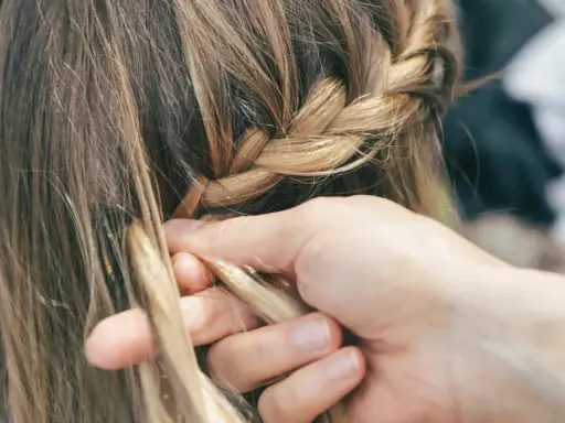 Mani esperte creano trecce alla francese, intrecciando ciocche bionde con cura.
