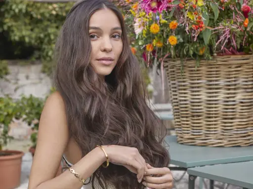 Donna con lunghi capelli mossi, un taglio butterfly a chi sta bene, con un cesto di fiori colorati sullo sfondo.