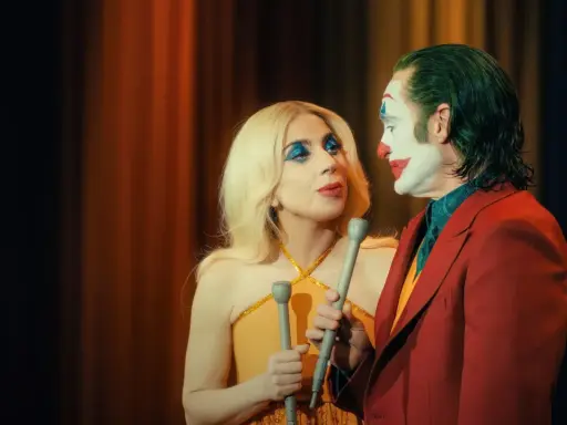 Joker e Harley Quinn, uniti dalla follia, si guardano intensamente. Lui con il trucco iconico, lei con un look scintillante. Joker folie a deux.