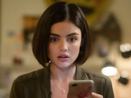 Lucy Hale, protagonista di film e programmi TV, guarda sorpresa il suo telefono.