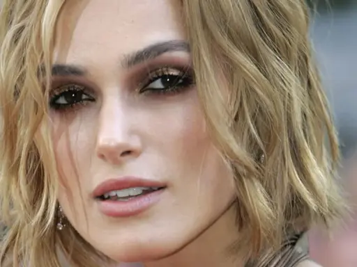 Primo piano di una donna con taglio butterfly capelli corti biondi, trucco occhi intenso e labbra rosa.