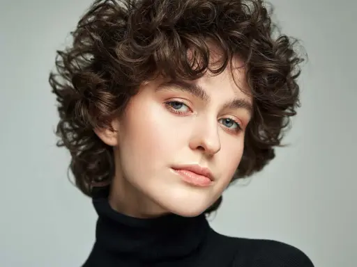 Modella con scalati tagli corti ricci, sguardo intenso e labbra naturali.