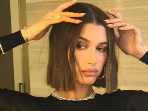 Modello con capelli castani, lisci e pochi, che sfoggia un taglio a caschetto. Indossa gioielli d'oro e un abito nero.