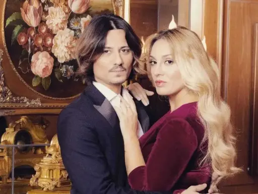 Francesca Manzini e il suo fidanzato, un abbraccio elegante davanti a un quadro di fiori e un orologio dorato.