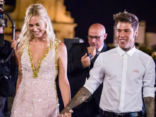 Fedez e Chiara sorridono, un momento speciale che ricorda la loro canzone. Lei indossa un abito scintillante, lui una camicia bianca.