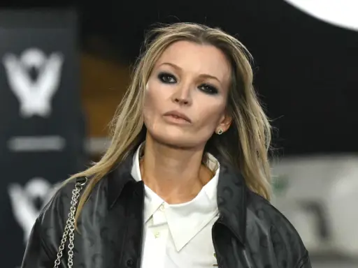 Kate Moss oggi, con un look audace e un trucco marcato, sfila con un giubbotto di pelle e una camicia bianca.