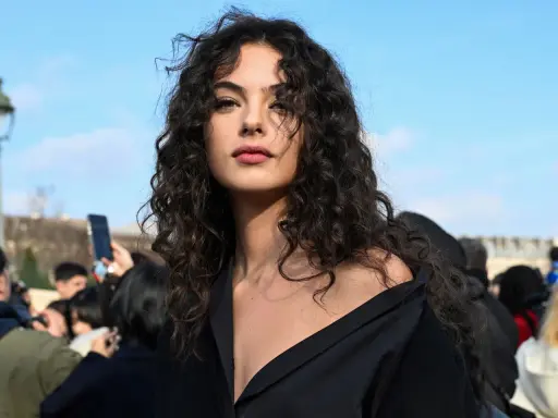 Ragazza con splendidi capelli ricci naturali con frangia, che incorniciano un viso intenso sotto un cielo azzurro.