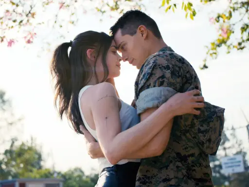 Nicholas Galitzine, in uniforme militare, abbraccia teneramente la sua fidanzata sotto un albero fiorito.