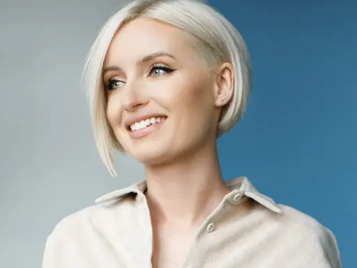 Donna sorridente con capelli sottili e pochi, taglio corto biondo platino e un orecchino a grappolo.