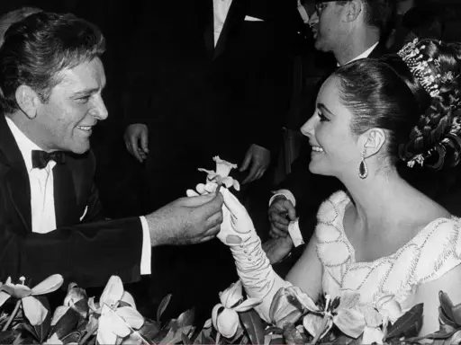 Richard Burton offre un fiore a Elizabeth Taylor, suo coniuge, in un momento di tenerezza tra fiori.