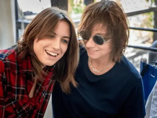 Due donne sorridono, una con camicia a quadri rossi, l'altra con occhiali da sole. Potrebbero essere Gianna Nannini e la sua moglie.