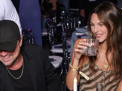 Vittoria Ceretti e Leonardo DiCaprio sorridono a una cena. Lei tiene un bicchiere, lui indossa un cappellino con la "LA".