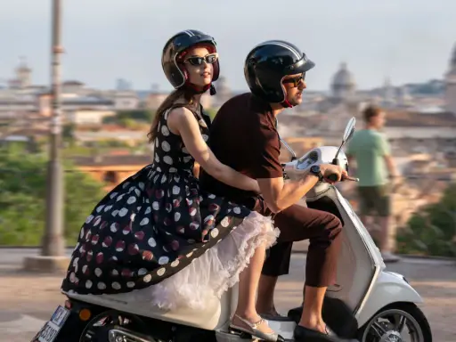 Emily in Paris 4: Emily e Gabriel sfrecciano su uno scooter a Roma, con la città sullo sfondo.