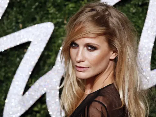 Donna con capelli sciolti eleganti, sguardo intenso e trucco deciso, sullo sfondo di un logo scintillante.
