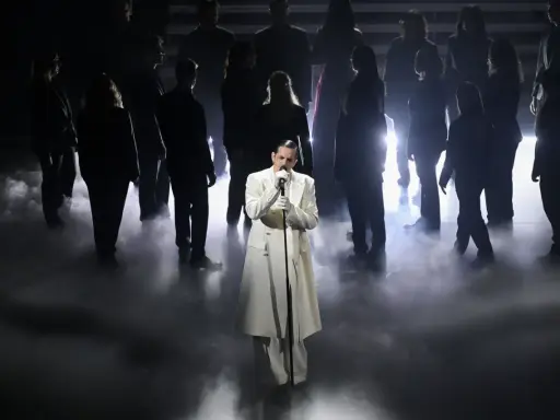 Achille Lauro, vestito di bianco, canta sul palco circondato da un coro in controluce, un'immagine che evoca un sentimento di essere perdutamente innamorato.