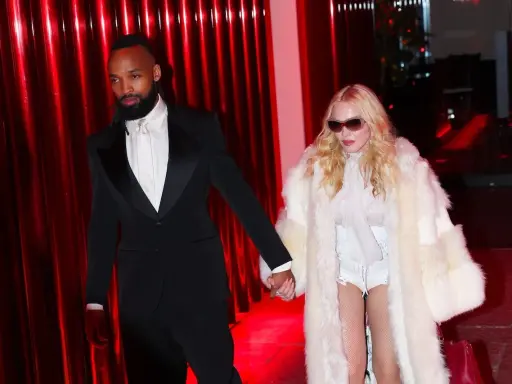 Madonna, con un cappotto di pelliccia bianco e un abito audace, cammina mano nella mano con il suo compagno, vestito elegantemente in smoking nero.