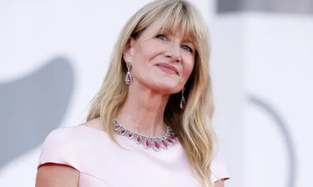 L'attrice bionda americana Laura Dern sorride con un abito rosa e gioielli scintillanti.