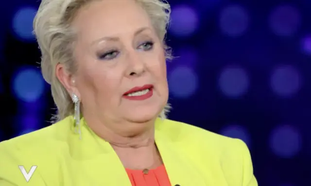 Carolyn Smith, come sta, con un tailleur giallo acceso e un top arancione, parla con un microfono.