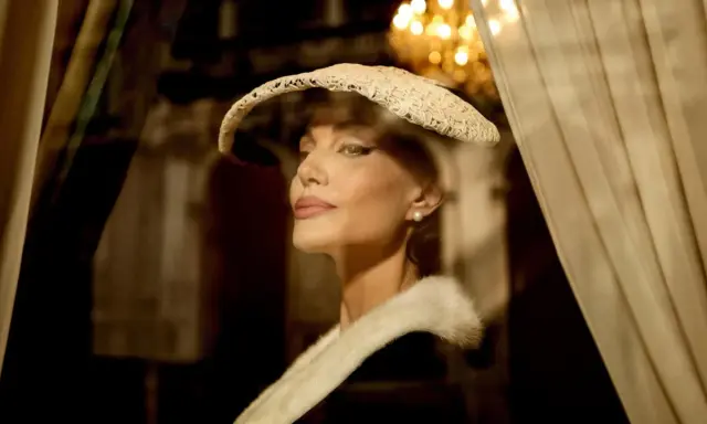 Angelina Jolie nei panni di Maria Callas, con un cappello di pizzo e una pelliccia, evoca l'eleganza di un'epoca passata.