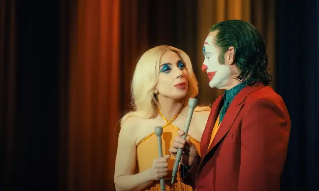 Joker e Harley Quinn, uniti dalla follia, si guardano intensamente. Lui con il trucco iconico, lei con un look scintillante. Joker folie a deux.