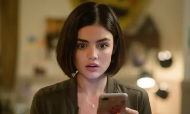 Lucy Hale, protagonista di film e programmi TV, guarda sorpresa il suo telefono.