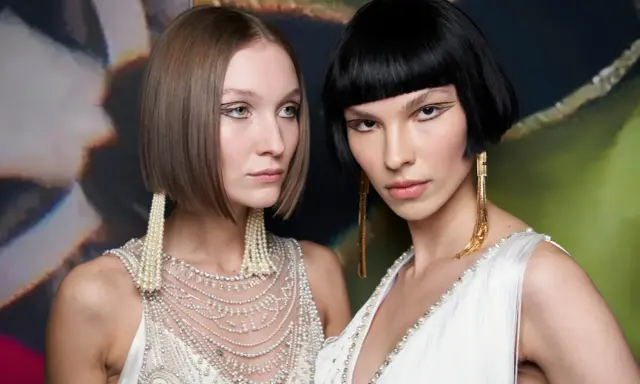 Due modelle con un sbarazzino caschetto corto sfilato, una con capelli castani e l'altra con capelli neri, sfoggiano orecchini pendenti e abiti decorati.