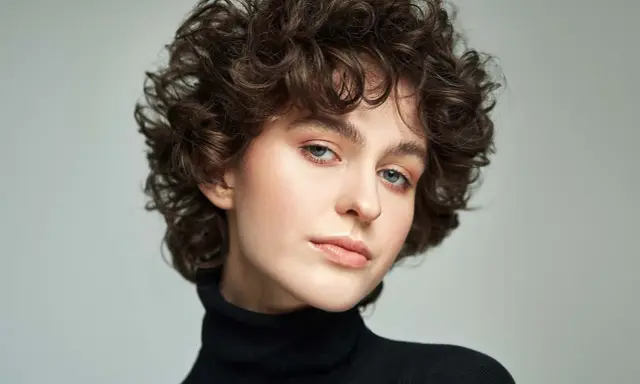 Modella con scalati tagli corti ricci, sguardo intenso e labbra naturali.