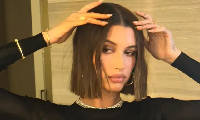 Modello con capelli castani, lisci e pochi, che sfoggia un taglio a caschetto. Indossa gioielli d'oro e un abito nero.