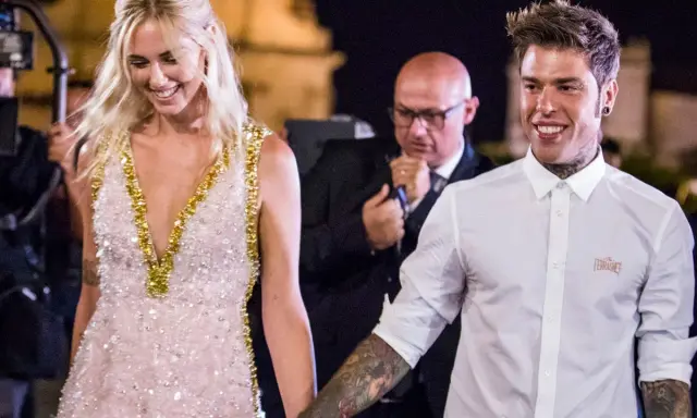 Fedez e Chiara sorridono, un momento speciale che ricorda la loro canzone. Lei indossa un abito scintillante, lui una camicia bianca.