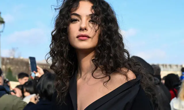 Ragazza con splendidi capelli ricci naturali con frangia, che incorniciano un viso intenso sotto un cielo azzurro.
