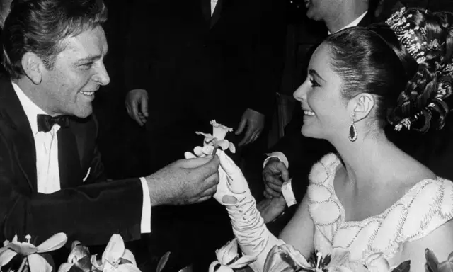 Richard Burton offre un fiore a Elizabeth Taylor, suo coniuge, in un momento di tenerezza tra fiori.