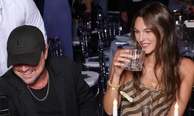Vittoria Ceretti e Leonardo DiCaprio sorridono a una cena. Lei tiene un bicchiere, lui indossa un cappellino con la "LA".
