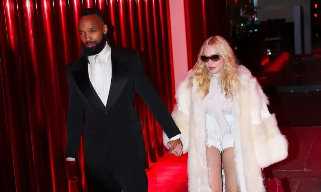 Madonna, con un cappotto di pelliccia bianco e un abito audace, cammina mano nella mano con il suo compagno, vestito elegantemente in smoking nero.